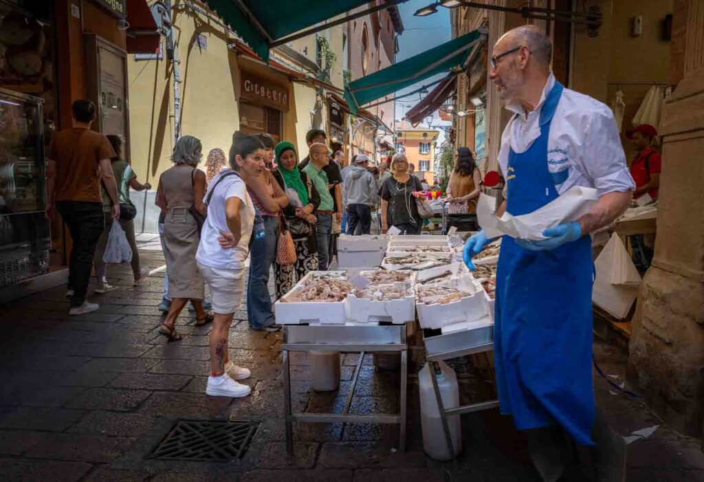 Fish vendor in a blue apron serving customers at an outdoor market stall.