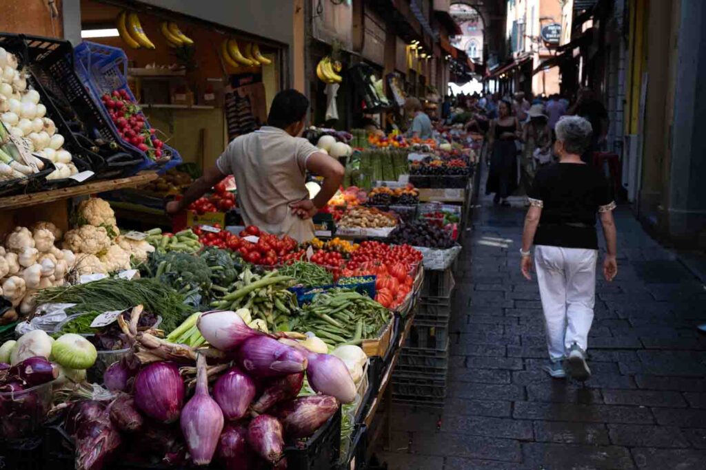 Narrow market street lined with stalls selling fresh vegetables and fruit.