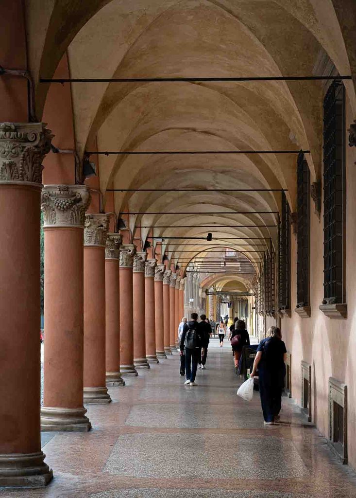 Pedestrians walking beneath Bologna's historic porticoes lined with Corinthian columns.