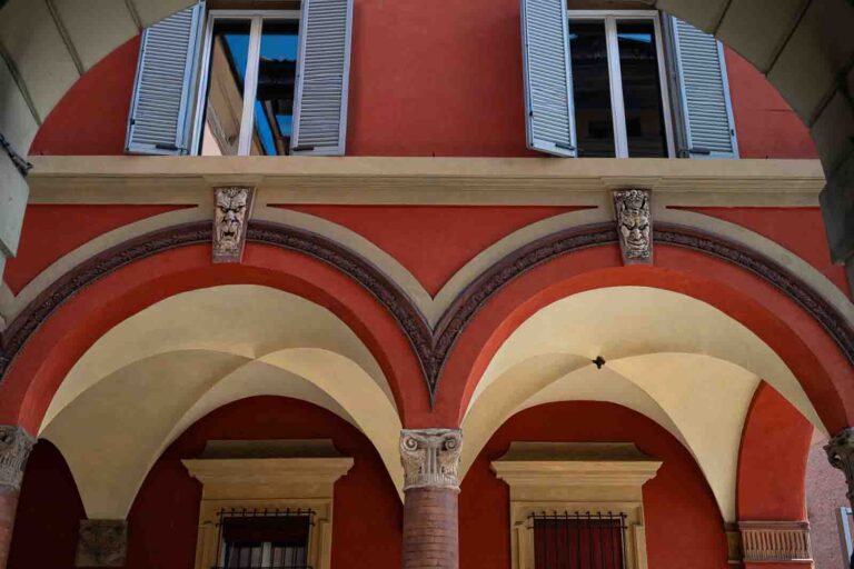 Interior courtyard with red walls, vaulted arches and masks in Bologna